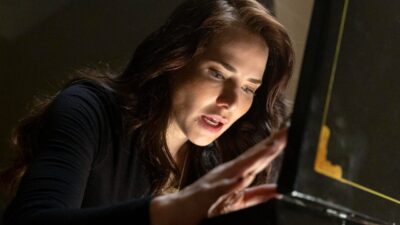 Adriana (Letícia Colin) observa e toca objeto iluminado com expressão concentrada em cena de Quem Ama Cuida
