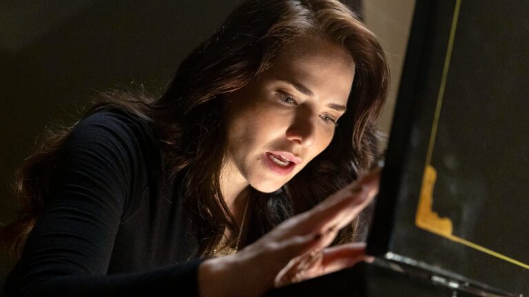 Adriana (Letícia Colin) observa e toca objeto iluminado com expressão concentrada em cena de Quem Ama Cuida