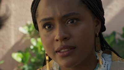 Alika/Lúcia (Duda Santos) com tranças e brincos longos olha apreensiva em cena da novela A Nobreza do Amor