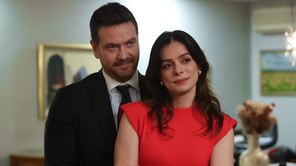 Bora (Engin Ozturk) de terno ao lado de Karsu (Ozge Ozpirincci) de vestido vermelho em cena de Coração de Mãe
