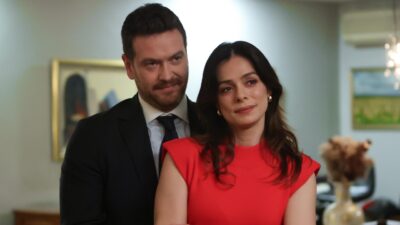 Bora (Engin Ozturk) de terno ao lado de Karsu (Ozge Ozpirincci) de vestido vermelho em cena de Coração de Mãe