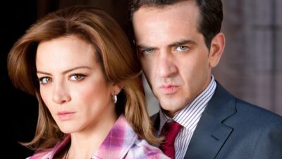 Camila Monterde (Silvia Navarro) em primeiro plano e Alonso (Flavio Medina) atrás com expressão séria em Amor Valente
