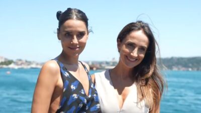 Cansu Dere e Patrícia Nielsen sorrindo lado a lado diante do mar em dia ensolarado