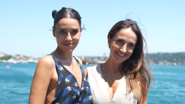 Cansu Dere e Patrícia Nielsen sorrindo lado a lado diante do mar em dia ensolarado