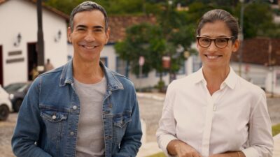 César Tralli de jaqueta jeans e Renata Vasconcellos de óculos e camisa branca sorriem em rua de Pirenópolis