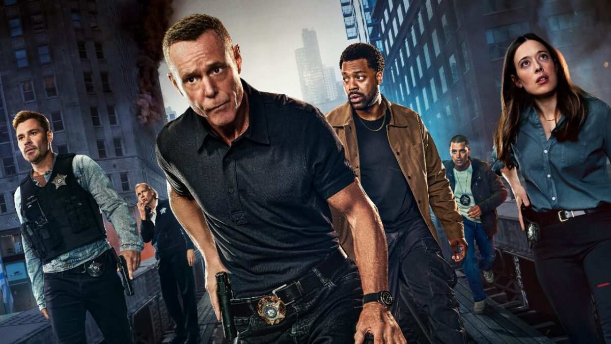 Elenco de Chicago P.D. posa como policiais em cenário urbano com prédios, fumaça e viatura ao fundo