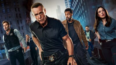 Elenco de Chicago P.D. posa como policiais em cenário urbano com prédios, fumaça e viatura ao fundo