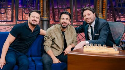 Clayton e Romário sorriem no sofá ao lado de Danilo Gentili, de terno, no cenário do programa The Noite