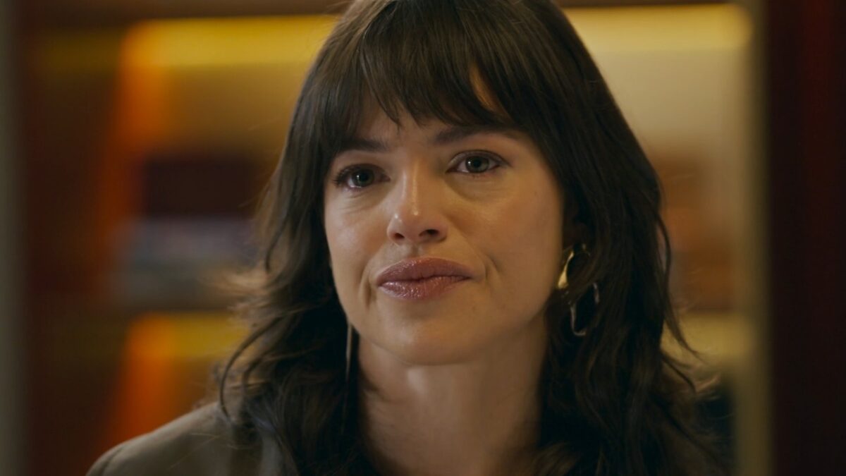 Ingrid (Agatha Moreira) com expressão séria e olhos marejados em ambiente interno na novela Quem Ama Cuida