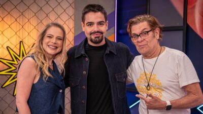 Jackeline Petkovic e João Silva sorriem ao lado de Roger Moreira, que aponta para o apresentador em estúdio