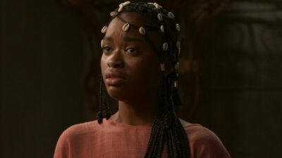 Kênia (Nikolly Fernandes) com tranças adornadas por búzios olha apreensiva em cena da novela A Nobreza do Amor
