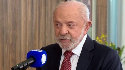 Lula de terno escuro e gravata vermelha fala diante de microfone azul da Record durante entrevista