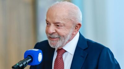 Lula de terno azul e gravata vermelha sorri diante de microfone durante entrevista à Record
