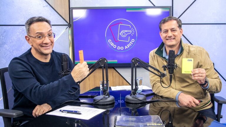 Maurício Noriega e Sálvio Spinola exibem cartões diante de microfones no estúdio do Giro do Apito