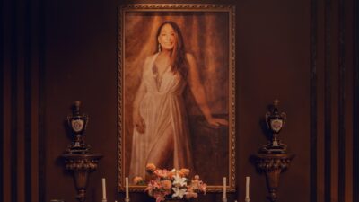 Retrato da Falecida (Susana Vieira) emoldurado sobre altar com flores e velas no reality Herança em Jogo