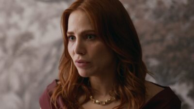 Adriana (Leticia Colin) olha apreensiva para o lado, com cabelos ruivos e vestido vinho em cena de Quem Ama Cuida