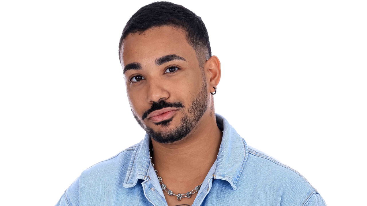 Albry Anunciação de camisa jeans e corrente prateada posa diante de fundo branco em Herança em Jogo