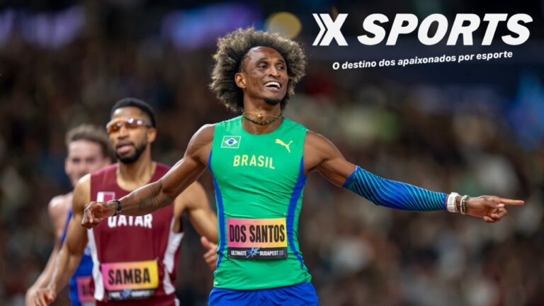 Alison dos Santos sorri com uniforme verde do Brasil e braços abertos após prova de atletismo, com adversários ao fundo