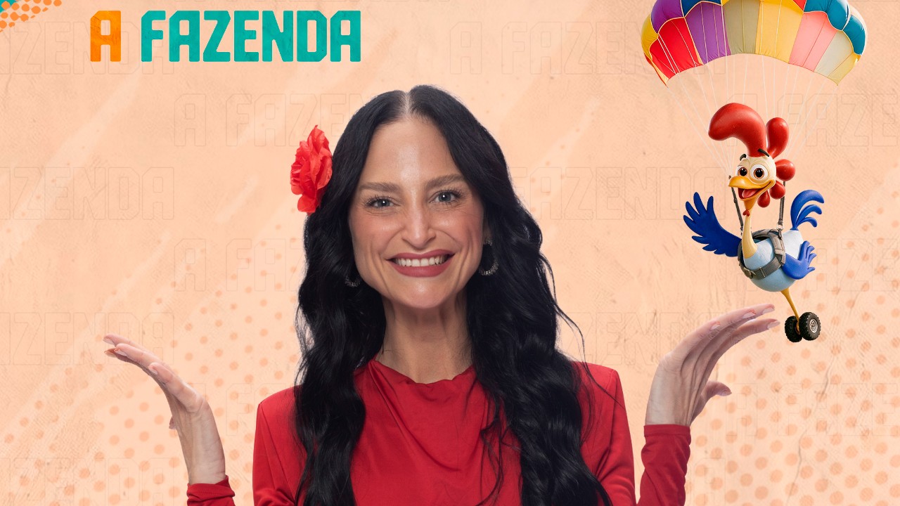 Ariela Carasso sorri de vermelho com flor no cabelo e mãos abertas diante do logo de A Fazenda