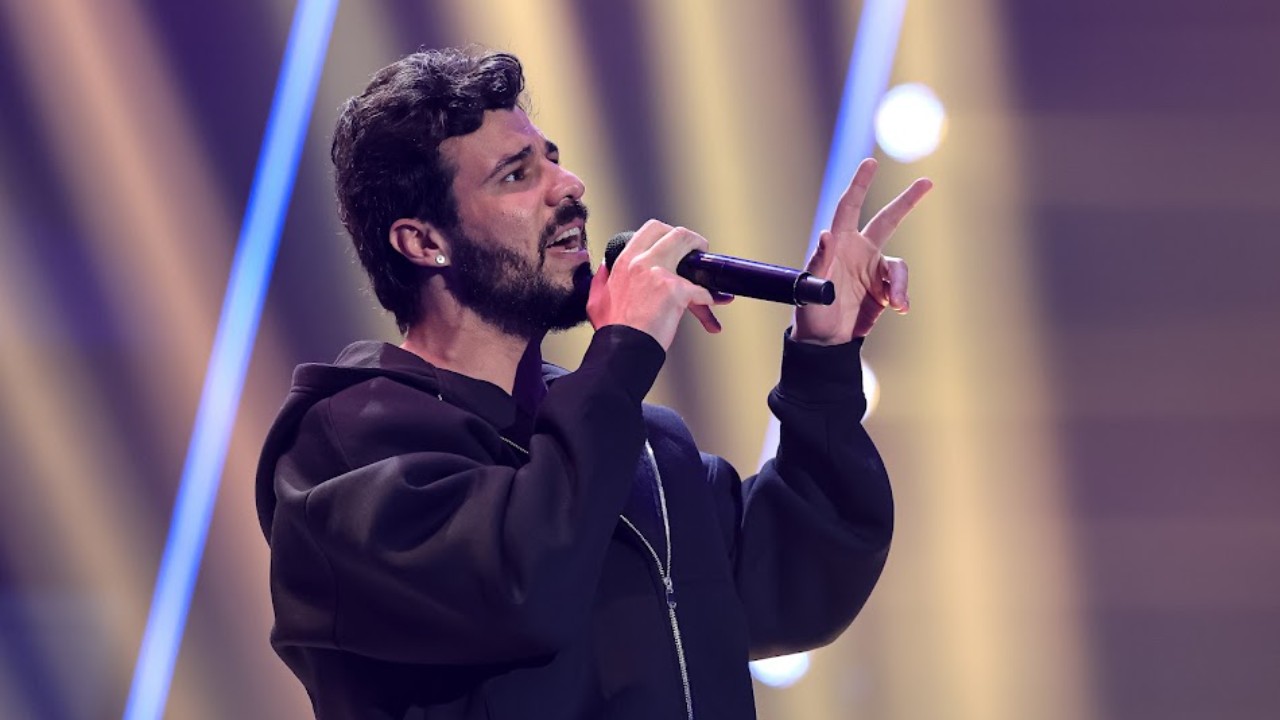Bidesão canta ao microfone de moletom preto durante as Audições às Cegas do The Voice Brasil