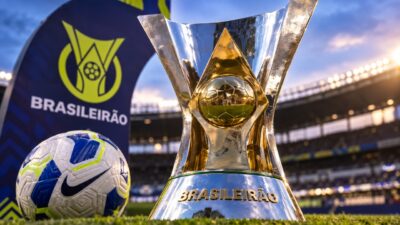 Troféu e bola do Campeonato Brasileiro no gramado de estádio com logotipo do Brasileirão ao fundo