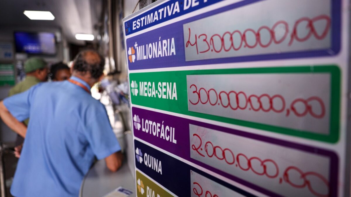 Painel em casa lotérica exibe prêmios da +Milionária, Mega-Sena e Lotofácil, com clientes ao fundo
