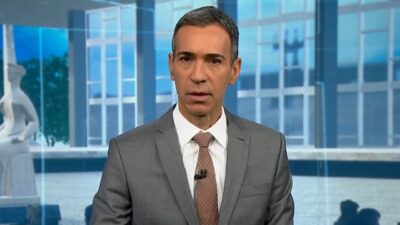 César Tralli de terno cinza e gravata apresenta o Jornal Nacional com imagem do STF ao fundo