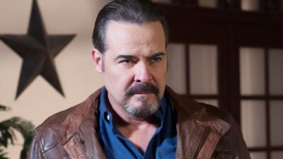 Dionisio Ferrer (César Évora) de jaqueta marrom encara alguém em cena da novela Amor Valente