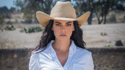 Fernanda Linhares (Livia Brito) de chapéu e camisa clara encara a câmera em cenário rural de A Desalmada