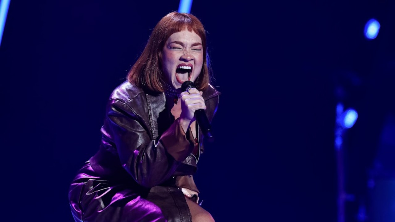 Jade Baraldo canta ao microfone com jaqueta de couro durante as Audições às Cegas do The Voice Brasil