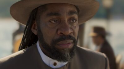 Jendal (Lázaro Ramos) de chapéu marrom, barba e tranças, com olhar sério em cena de A Nobreza do Amor
