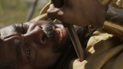 Jendal (Lázaro Ramos) caído no chão segura a lança que o atingiu no peito em cena de A Nobreza do Amor
