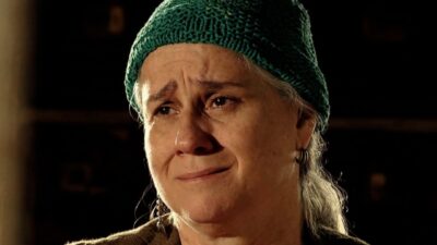 Lucinda (Vera Holtz) de gorro verde com olhos marejados e expressão de choro em cena de Avenida Brasil