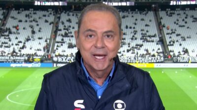 Luís Roberto de jaqueta azul e headset fala diante do gramado e das arquibancadas da Neo Química Arena