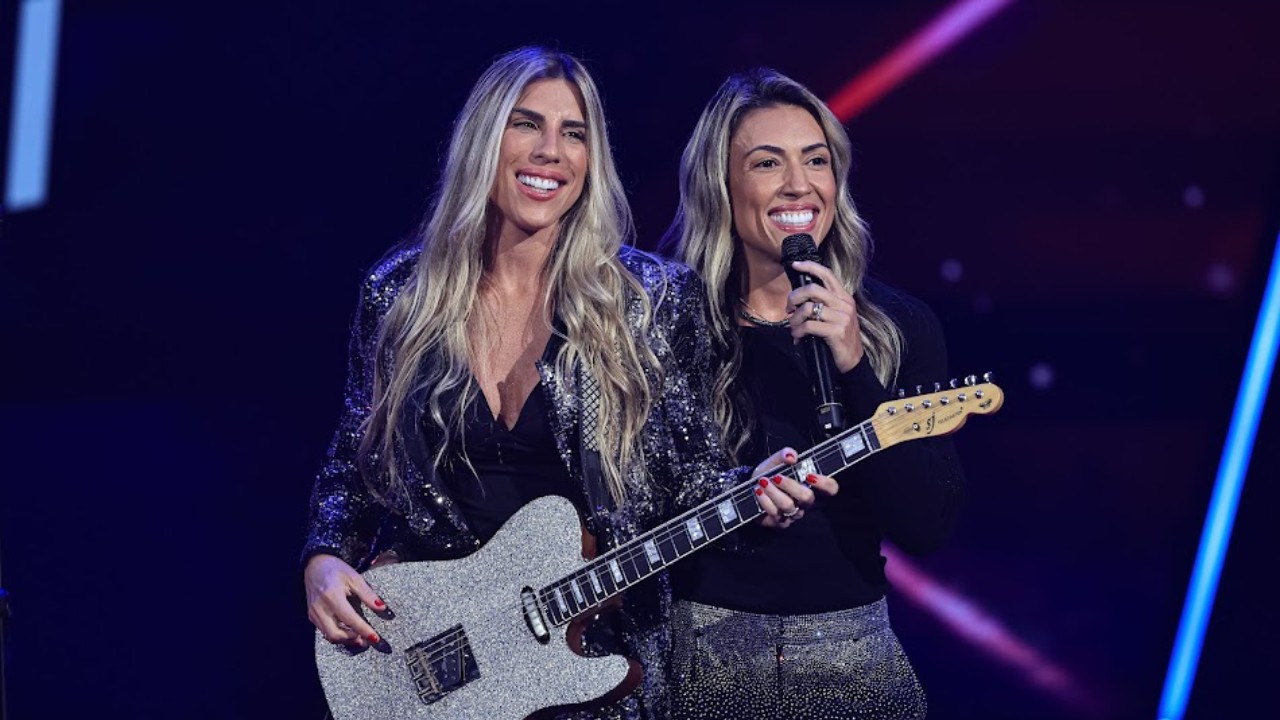 Marcela Martinez e Luene Carvalho, do MaLuê, sorriem com guitarra e microfone no palco do The Voice Brasil