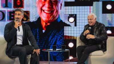 Marcos Mion e Antonio Fagundes sentados com microfones no palco do Caldeirão com Mion