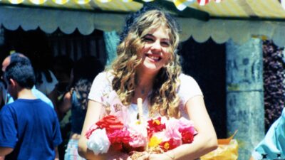 Marisol (Bárbara Paz) sorri enquanto segura cesta com flores coloridas em feira ao ar livre