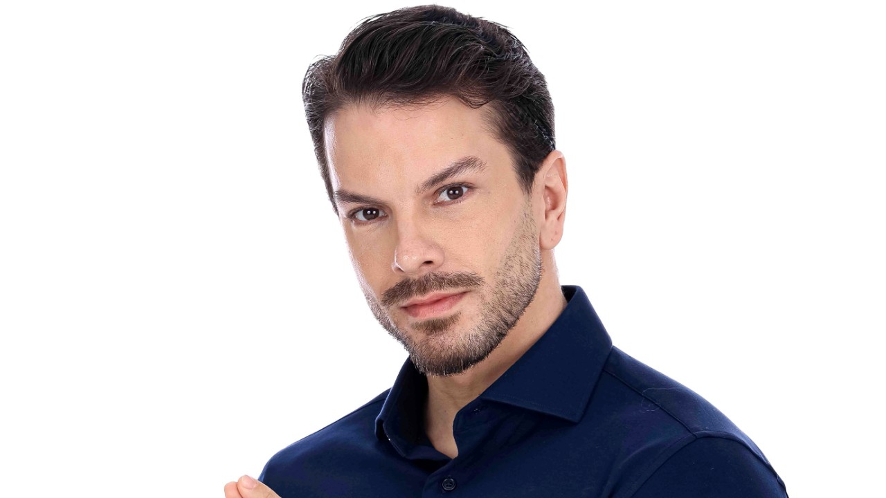 Mike Nunes posa de camisa azul-marinho, com barba curta e cabelo escuro, diante de fundo branco em Herança em Jogo