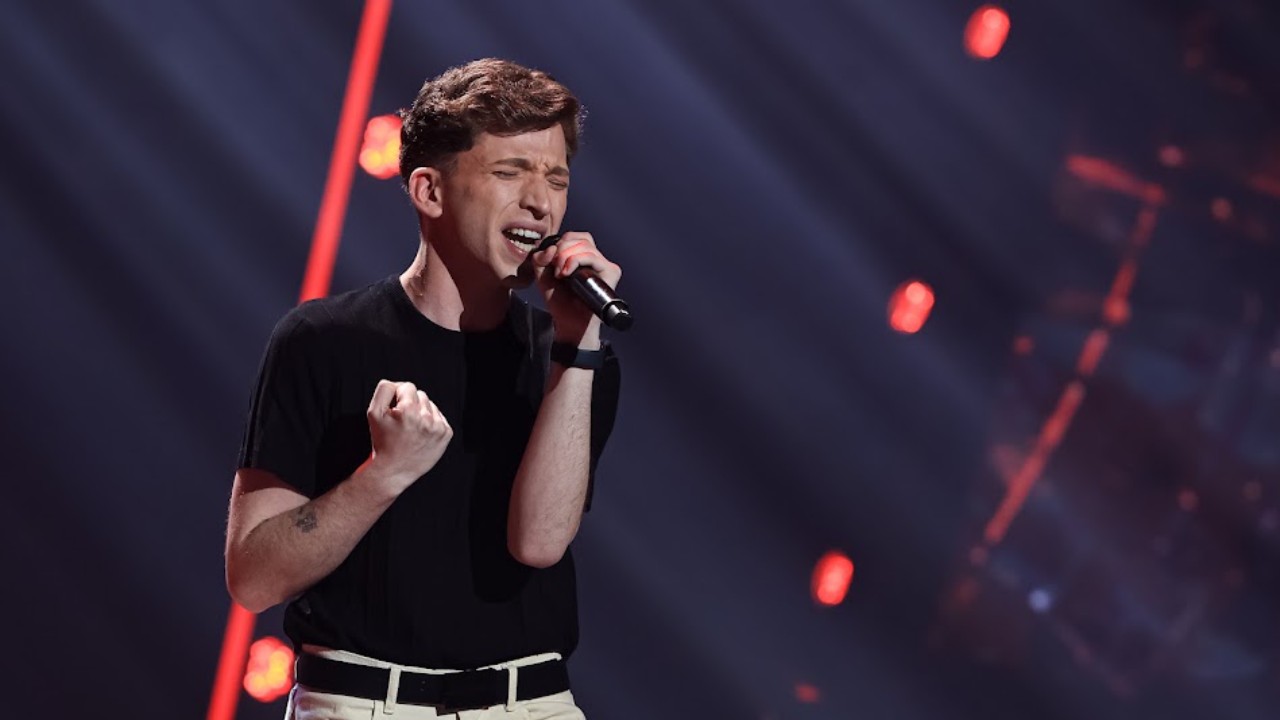 Paulo Bentes canta ao microfone de camiseta preta durante as Audições às Cegas do The Voice Brasil
