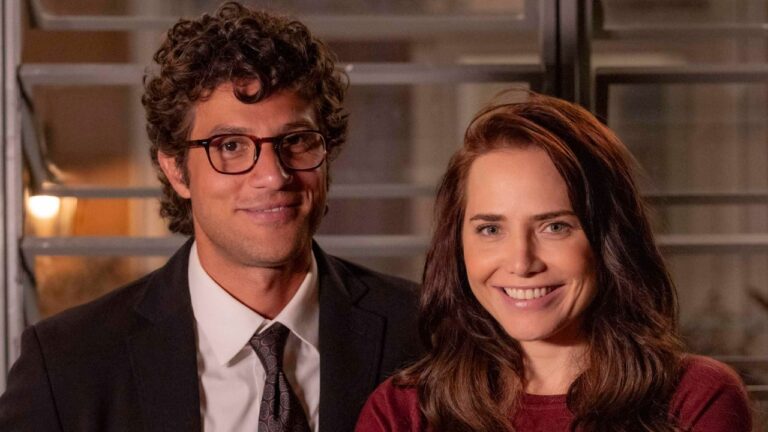 Pedro (Chay Suede) de terno e Adriana (Leticia Colin) de blusa vinho sorriem lado a lado em Quem Ama Cuida