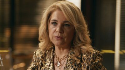 Pilar (Isabel Teixeira) de blazer dourado e colares, com expressão séria, em cena de Quem Ama Cuida