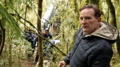 Roberto Cabrini de casaco escuro em área de mata durante gravação com equipe ao fundo