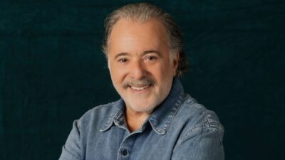 Tony Ramos sorrindo de camisa jeans em retrato com fundo escuro