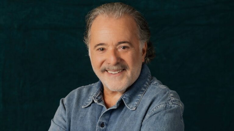 Tony Ramos sorrindo de camisa jeans em retrato com fundo escuro