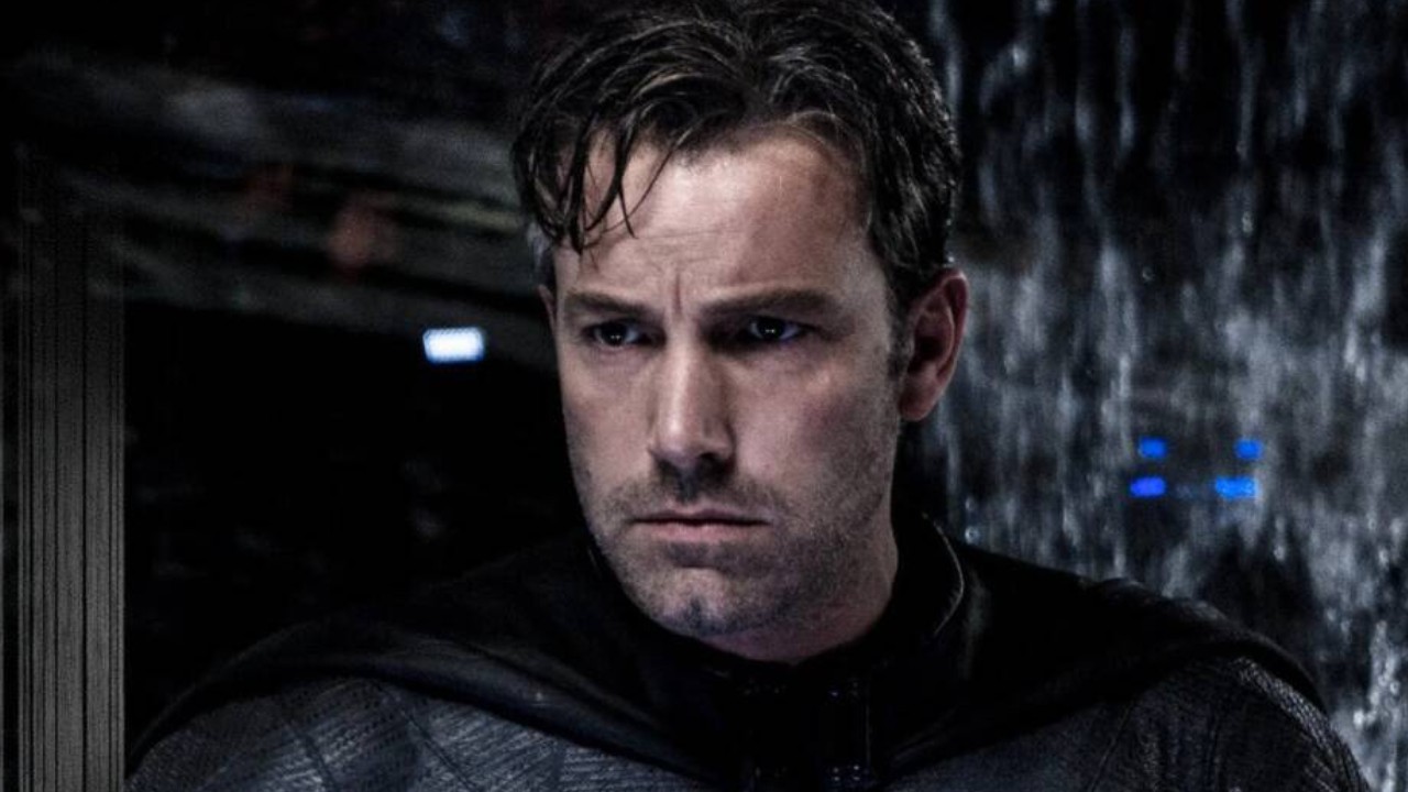 Ben Affleck aparece caracterizado como Batman, com uniforme preto, capa e expressão séria, em uma cena de ambiente escuro