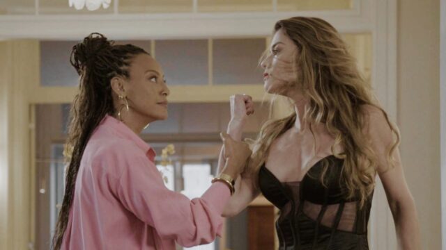 Bela (Sheron Menezzes), de camisa rosa, segura o braço de Vanessa (Alinne Moraes), vestida de preto, durante confronto em cena da novela Por Você