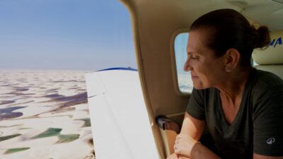 Bette Lucchese olha pela janela de um avião, com dunas e lagoas dos Lençóis Maranhenses ao fundo