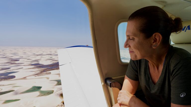 Bette Lucchese olha pela janela de um avião, com dunas e lagoas dos Lençóis Maranhenses ao fundo