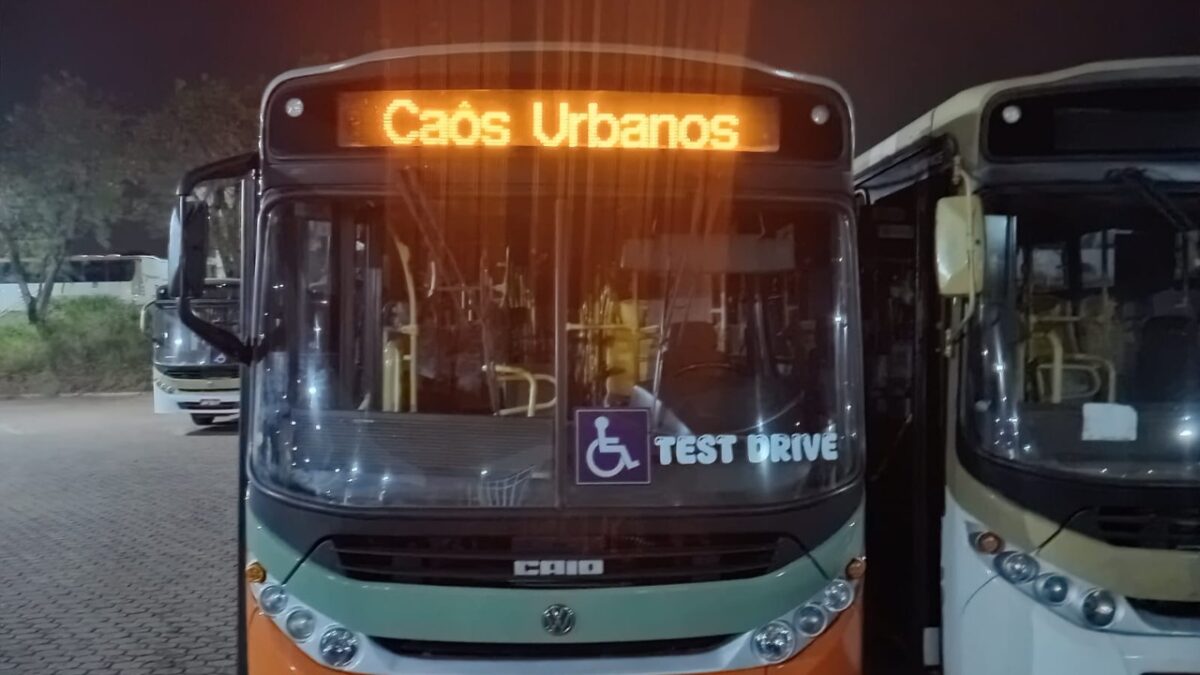 Ônibus estacionado à noite exibe Caôs Urbanos no letreiro, adesivo Test Drive e símbolo de acessibilidade