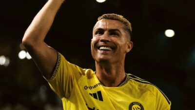 Cristiano Ronaldo sorri e levanta o braço com a camisa amarela do Al-Nassr durante partida de futebol